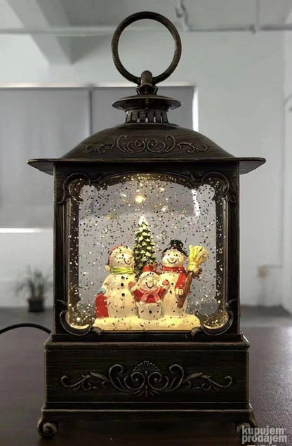 Novogodišnji ukras u obliku lampe prikazuje Deda Mraza sa jelkom.
